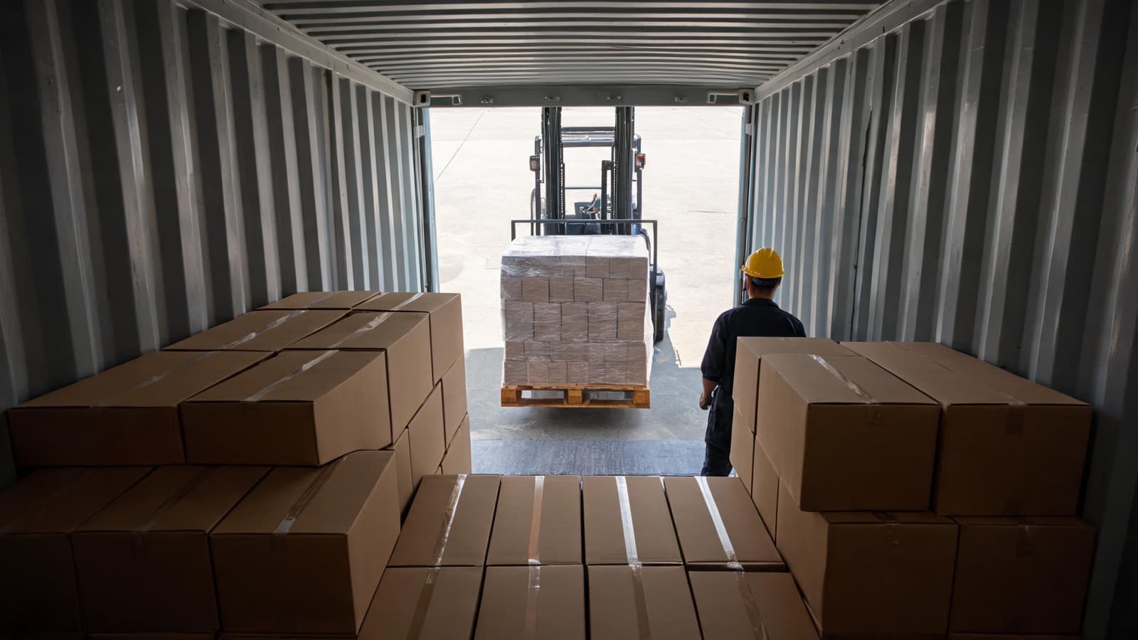 Forklift moving a stretch-wrapped pallet of plain cartons into a 40HQ container